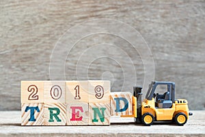 Toy forklift hold letter block d to word 2019 trend on wood background