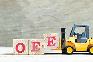 Toy forklift hold block E to complete word OEE abbreviation of overall equipment effectiveness on wood background photo