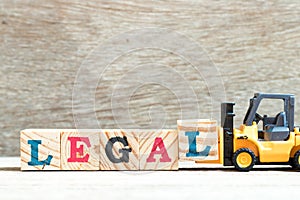 Toy forklift hold letter block l to word legal on wood background