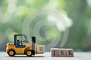 Toy forklift hold letter block R to complete word RISK