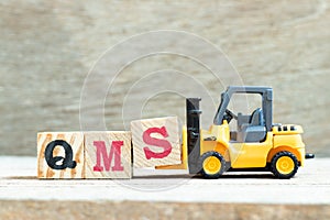 Toy forklift hold block S to complete word QMS abbreviation of quality management system on wood background photo