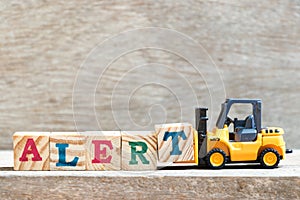 Toy forklift hold letter block T to word alert on wood background