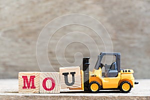 Toy forklift hold letter u in word mou abbreviation of memorandum of understanding on wood background