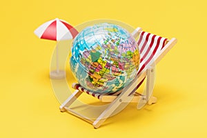 Toy globe in a deck chair on a yellow background. Concept on the topic: how long the holidays in different countries last photo