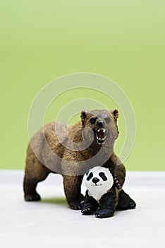 A toy grizzly bear protects a toy little panda
