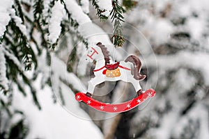 Toy horse on a snow-covered fir branch. Christmas tree in the snow and Christmas decorations. Christmas card