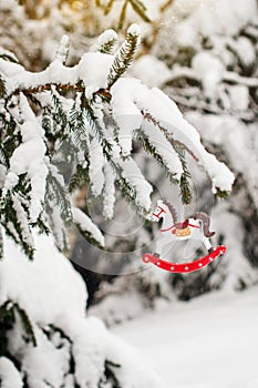 Toy horse on a snow-covered fir branch. Christmas tree in the snow and Christmas decorations. Christmas card