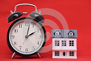 Toy house and black alarm clock isolated on red background. Mortgages and home purchases.