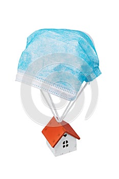 Toy house flies on a parachute from a medical mask isolated on a white background. Concept on a safe place during a pandemic