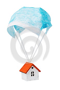 A toy house is flying on a parachute from a medical mask, isolated on a white background. Quarantine exit concept