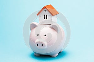 Toy house and piggy bank on a blue background. Concept of accumulating money to buy a house