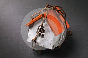 A toy house wrapped in a chain on a dark background. The concept of the arrest of property for tax evasion photo