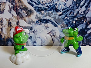 Toy from kinder surprise green frogs on the background of a snowy forest. Hobby. Kinderfilia - collecting children`s toys