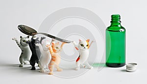 Toy kittens carry a teaspoon to an open green bottle with medicinal syrup. Playful concept of teaching children to use medicines