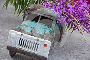 toy metal machine with traces of corrosion. Rust on the machine's gland. Flowers of fireweed by car