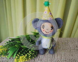 Toy mouse in party hat. Standing about with a branch of yellow f