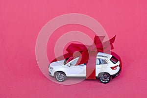 Toy new car gift with red bow on red background. Concept rental, auto dealership, copy space