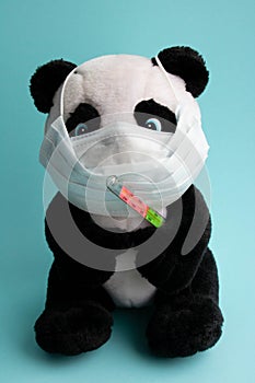 A toy panda in a medical mask with a thermometer sits on ablue background. Coronavirus treatment concept