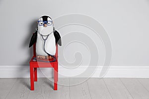 Toy penguin with eyeglasses and stethoscope near wall, space for text. Pediatrician practice