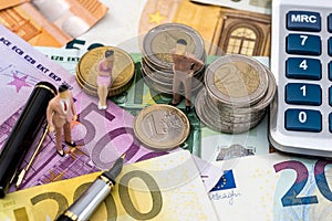 Toy people sit on euro coin with calculator, pen and euro bills