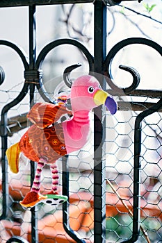 Toy pink flamingo hangs on a metal balcony railing. Close-up