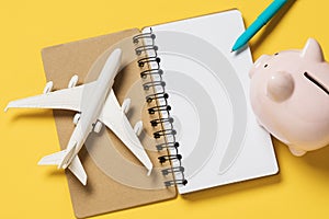 Toy plane, notebook and piggy bank on a yellow background. Concept on saving money on flights