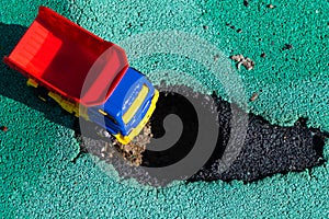 Toy plastic truck with a red body stopped in front of the pit. The car can not go. Hole on asphalt. The road needs