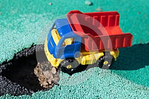 Toy plastic truck with a red body stopped in front of the pit. The car can not go. Hole on asphalt. The road needs
