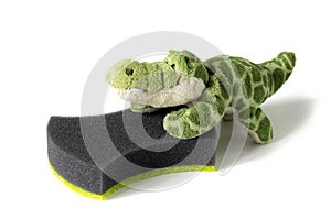 Toy plush crocodile pushes black sponge for household needs on white background. Concept of involving children in