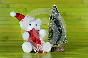 Toy polar bear cub with a hat and a red scarf sitting next to a decorative chrismas tree on green wood background