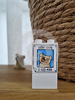 Toy poster of a lost dog. Part of a Lego duplo. Lost dog stands literally behind the poster. Kid toys