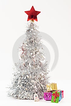 Toy puppy and colorful gift boxes under the Christmas silver tree with a red star on the top