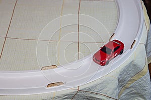 Toy red car rides along the ring track on the table. Kids games at home. Slot car racing track with small sport car