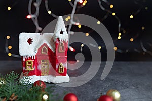 Toy red Christmas house with snow on the roof against the background of pink Christmas lights. Greeting card template christmas