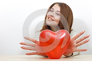 Toy red heart. Girl holds her heart in front. Holds fingers in the shape of angel wings. Valentines Day. Happy smiling young woman