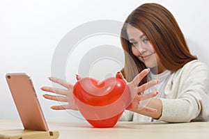 Toy red heart. Girl holds her heart in front of phone screen. Talking on  Internet. Valentines Day, communication by videoconferen