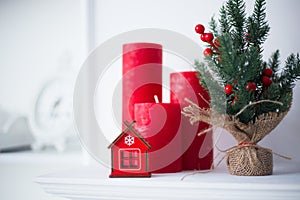 Toy red winter house in home festive interior with Christmas candles and white wall on background