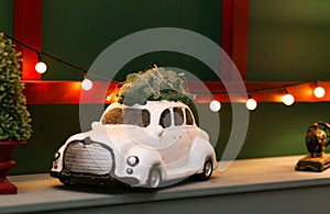 A toy retro car carrying a christmas tree stands on a shelf against the background of a christmas garland