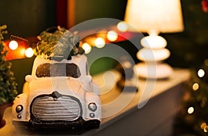 A toy retro car carrying a christmas tree stands on a shelf against the background of a christmas garland