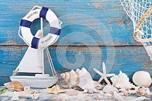 Toy sailboat and life buoy with seashells and starfish an a wood