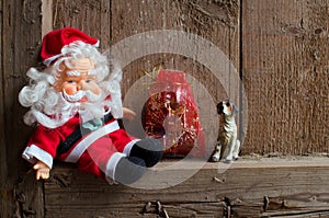 Toy Santa Claus figurine dog and a bag with Christmas gifts on vintage wooden background.