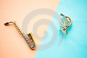 Toy saxophone and french horn on geometric blue and pink background