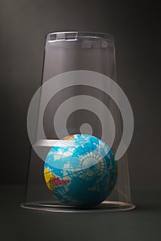 Toy in the shape of a globe is covered with a plastic glass. Concept on the topic of clogging the planet with plastic