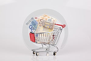 Toy shopping cart filled with euro notes on white background