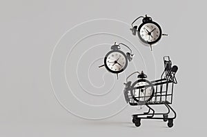 Toy shopping cart with three levitating alarm clocks on gray background with copy space. Black Friday banner, shopping concept