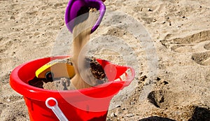 Toy shovel adding sabd to yellow toy car inside bucket on  beach