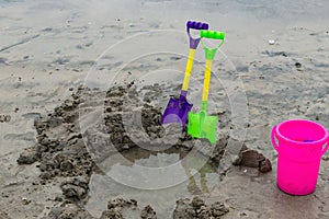 Toy shovels and bucket with a hole on a beach