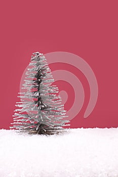 Toy silver Christmas tree on artificial white snow against pink background
