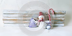 Toy snowman, caramel stick, Christmas decorations on a light wooden background