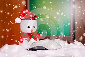 Toy snowman in front of a computer mouse on the background of the computer, there is snow. Greetings with Merry Christmas and New